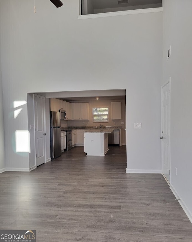 unfurnished living room with a ceiling fan, dark wood-style flooring, a towering ceiling, and baseboards