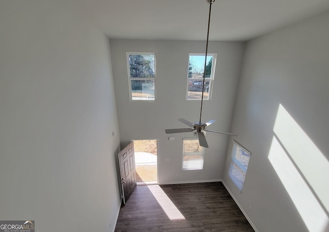 interior space with dark wood-type flooring, a ceiling fan, a high ceiling, and baseboards