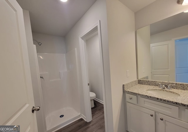 bathroom featuring toilet, a stall shower, wood finished floors, and vanity