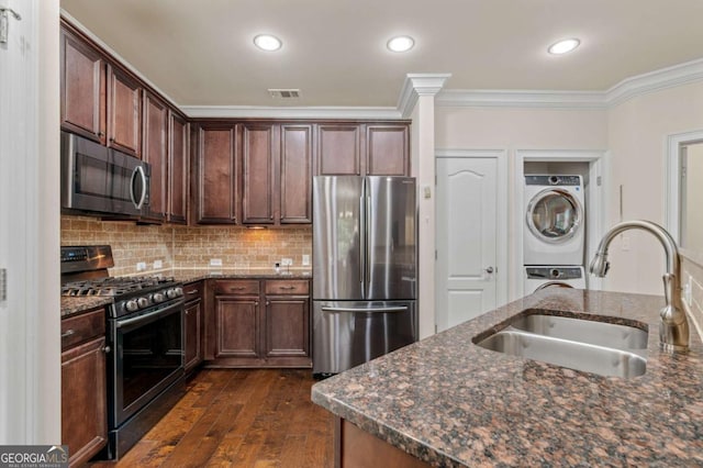 kitchen with visible vents, stacked washer and clothes dryer, appliances with stainless steel finishes, ornamental molding, and a sink