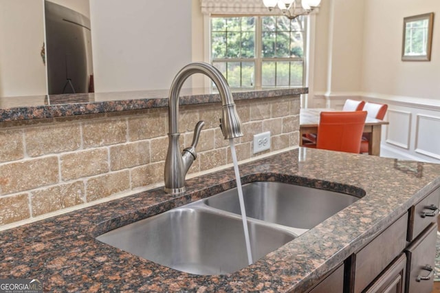 details with a decorative wall, a sink, wainscoting, dark stone countertops, and an inviting chandelier