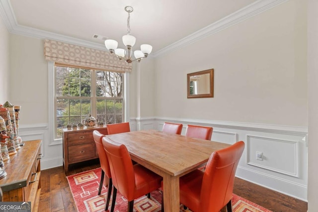 dining area with dark wood-style floors, crown molding, visible vents, an inviting chandelier, and wainscoting