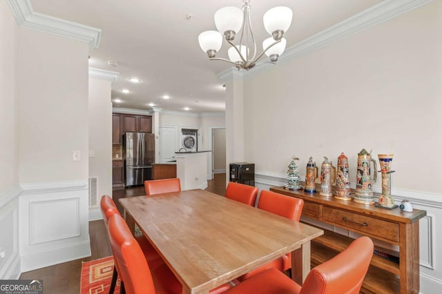 dining space with dark wood finished floors, wainscoting, stacked washer / drying machine, an inviting chandelier, and crown molding