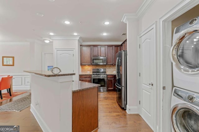 kitchen with light wood finished floors, stainless steel appliances, crown molding, stacked washing maching and dryer, and backsplash