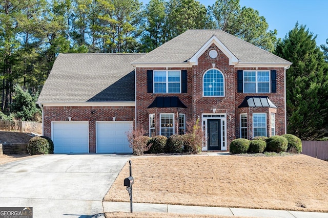 colonial inspired home with an attached garage, brick siding, fence, driveway, and roof with shingles