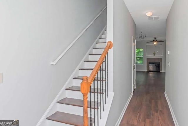 stairs featuring wood finished floors, a ceiling fan, visible vents, baseboards, and a glass covered fireplace