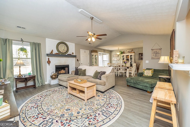 living room featuring a fireplace with raised hearth, lofted ceiling, wood finished floors, a ceiling fan, and visible vents