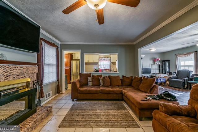 living area with light tile patterned floors, ceiling fan, visible vents, and crown molding