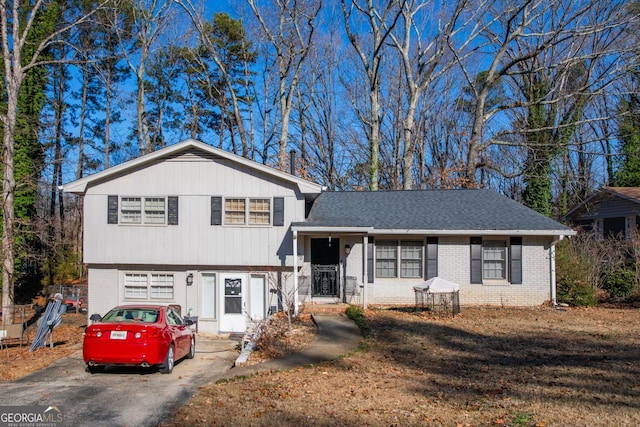 tri-level home with driveway, brick siding, and roof with shingles