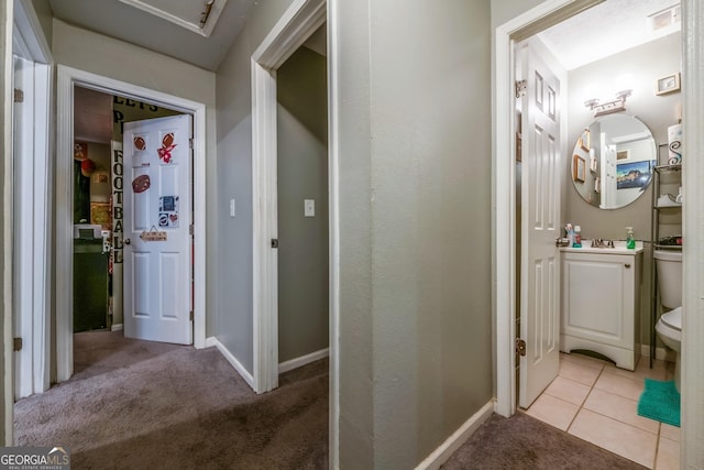 hall with light tile patterned floors, baseboards, visible vents, light colored carpet, and a sink