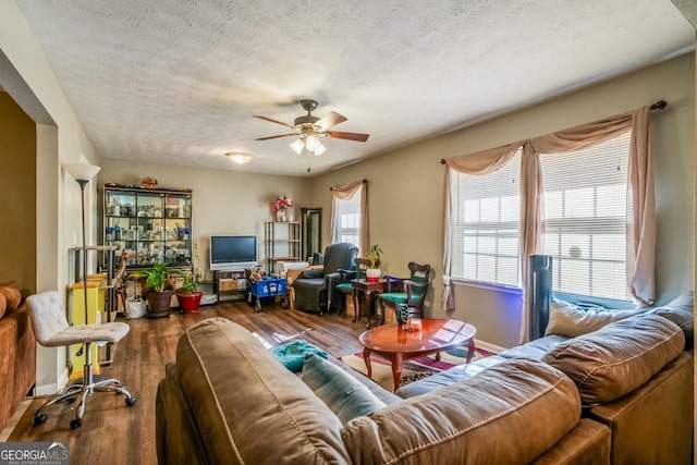 living area featuring ceiling fan, a textured ceiling, baseboards, and wood finished floors