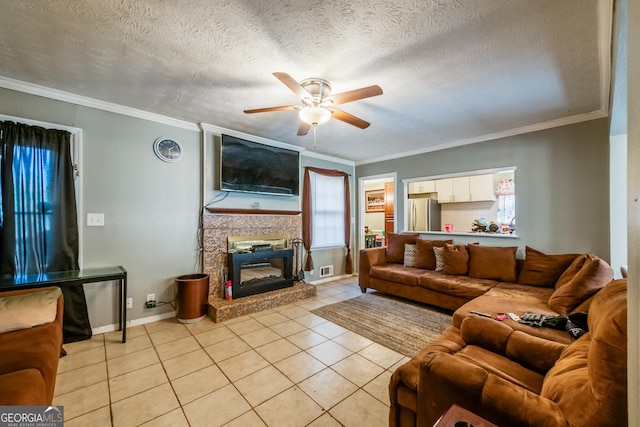 living area featuring light tile patterned floors, a textured ceiling, a ceiling fan, ornamental molding, and a glass covered fireplace