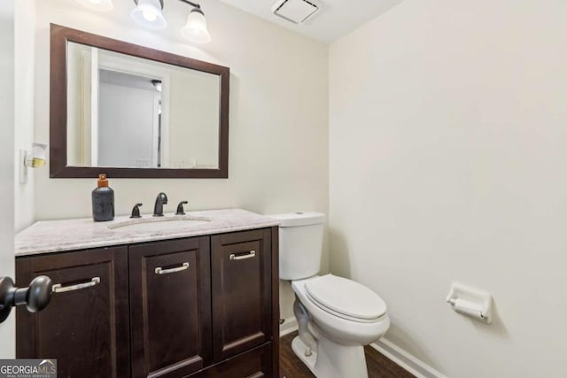 half bath featuring visible vents, vanity, toilet, and baseboards