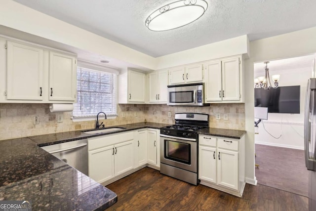 kitchen featuring a sink, appliances with stainless steel finishes, backsplash, dark wood-style floors, and dark stone countertops