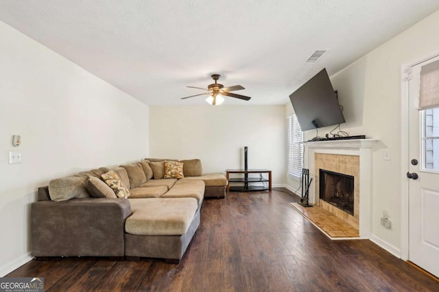 living room with ceiling fan, hardwood / wood-style flooring, a tiled fireplace, and visible vents