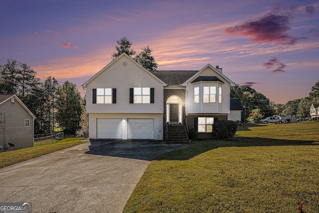 raised ranch with brick siding, a yard, fence, a garage, and driveway