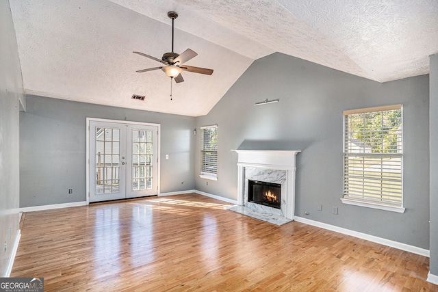 unfurnished living room with wood finished floors, french doors, vaulted ceiling, and a premium fireplace