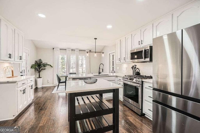 kitchen with decorative backsplash, appliances with stainless steel finishes, a peninsula, white cabinetry, and a sink