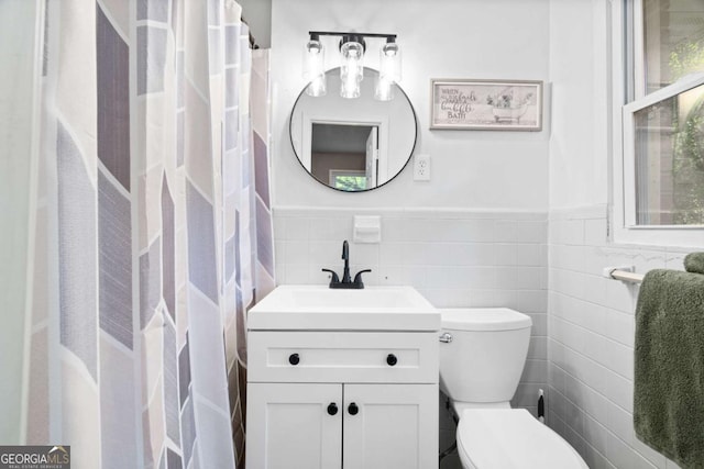 bathroom with a wainscoted wall, vanity, toilet, and tile walls