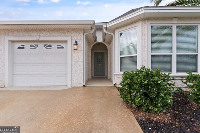 entrance to property featuring a garage, driveway, and stucco siding