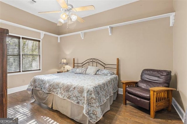 bedroom with a ceiling fan, visible vents, baseboards, and wood finished floors