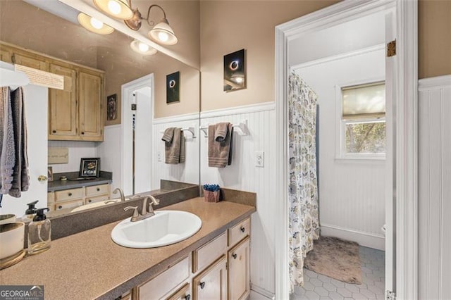 full bath featuring a shower with shower curtain, tile patterned flooring, vanity, and wainscoting