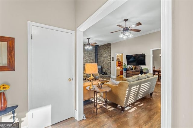 living area with a wood stove, crown molding, a ceiling fan, and wood finished floors