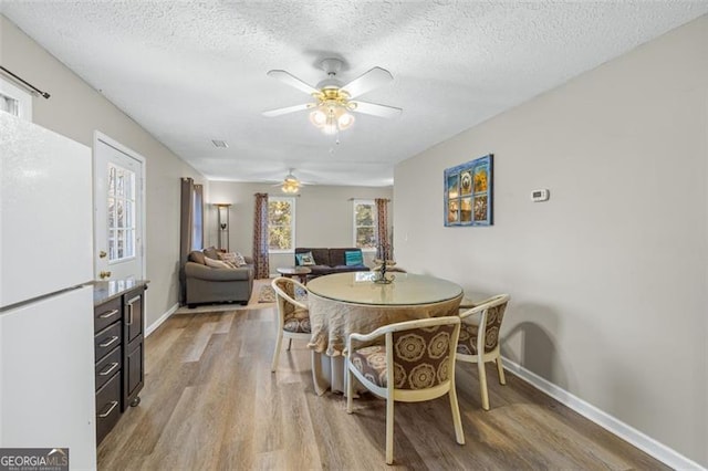 dining area with light wood-type flooring, visible vents, baseboards, and a textured ceiling