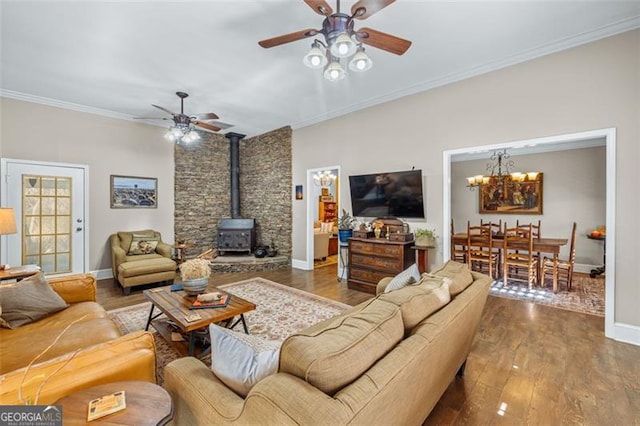 living room featuring a wood stove, ornamental molding, wood finished floors, and ceiling fan with notable chandelier