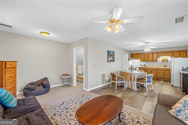 living area featuring a ceiling fan, baseboards, visible vents, and a textured ceiling