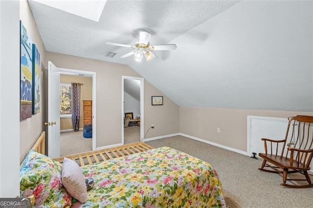 carpeted bedroom with visible vents, ceiling fan, a textured ceiling, vaulted ceiling with skylight, and baseboards