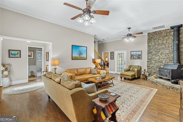 living room with visible vents, stairway, ornamental molding, wood finished floors, and a wood stove