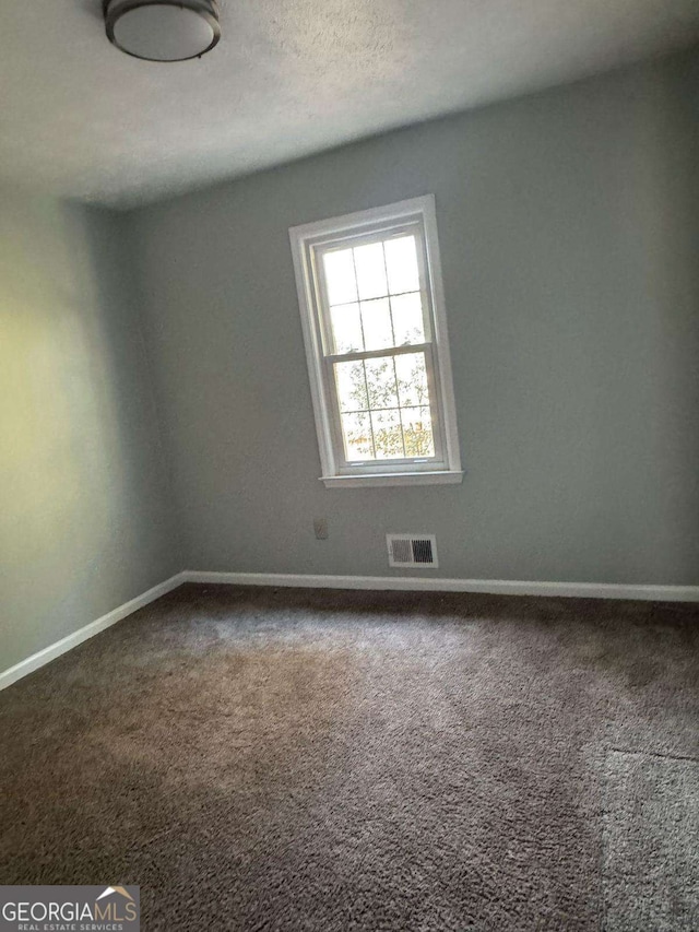 spare room featuring carpet floors, baseboards, visible vents, and a textured ceiling