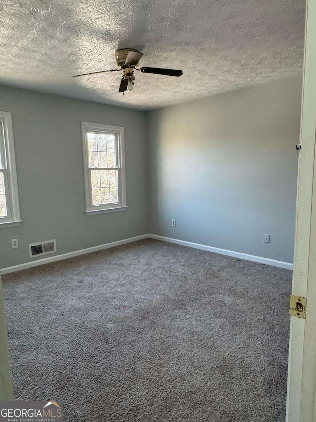 empty room featuring a textured ceiling, visible vents, baseboards, a ceiling fan, and carpet