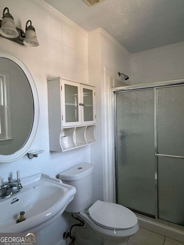 bathroom featuring toilet, a sink, tile patterned floors, a stall shower, and crown molding