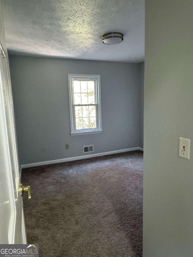 carpeted empty room with baseboards, visible vents, and a textured ceiling