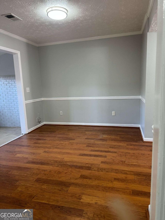 empty room featuring visible vents, a textured ceiling, ornamental molding, and wood finished floors