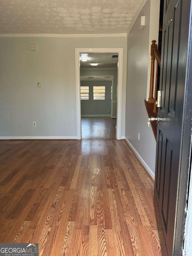 spare room featuring ornamental molding, a textured ceiling, baseboards, and wood finished floors