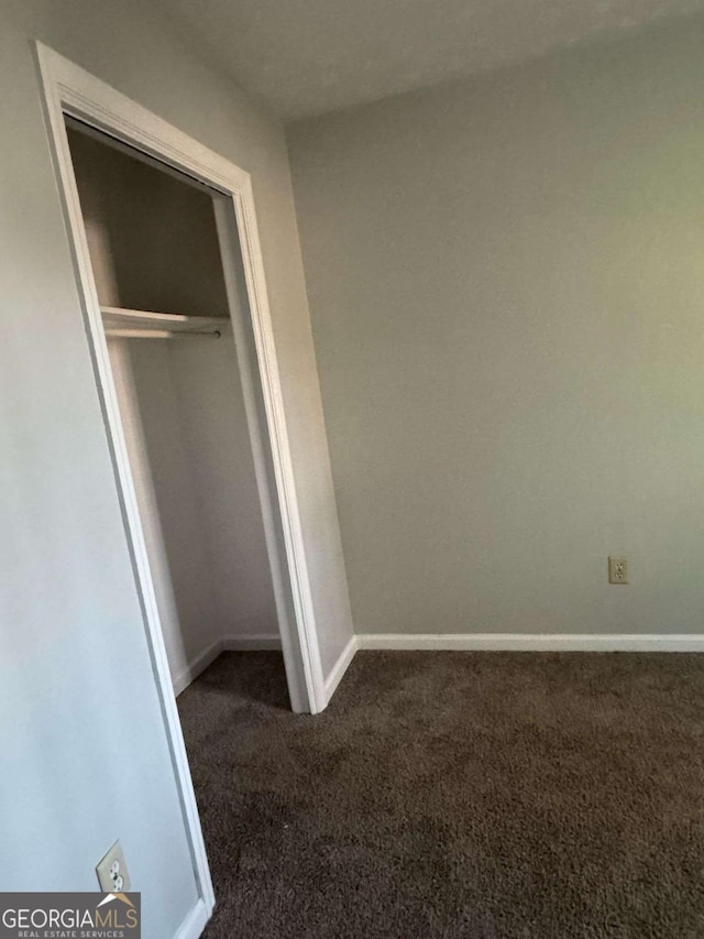 unfurnished bedroom with a closet, dark carpet, and baseboards