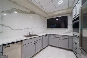 kitchen featuring appliances with stainless steel finishes, a sink, gray cabinets, a paneled ceiling, and backsplash