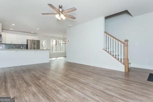 unfurnished living room featuring stairs, a ceiling fan, wood finished floors, and recessed lighting