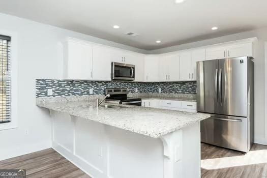 kitchen with tasteful backsplash, white cabinets, appliances with stainless steel finishes, wood finished floors, and a peninsula