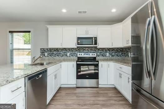 kitchen with wood finished floors, appliances with stainless steel finishes, a sink, and decorative backsplash