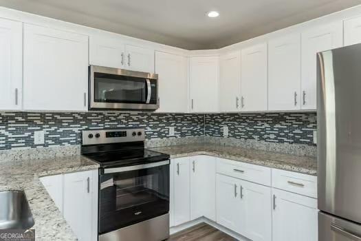 kitchen with tasteful backsplash, light stone countertops, stainless steel appliances, white cabinetry, and recessed lighting