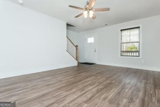 unfurnished living room featuring ceiling fan, stairway, and wood finished floors