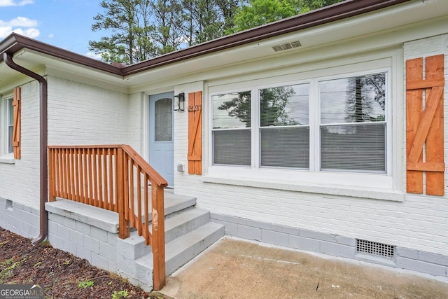 doorway to property featuring brick siding, visible vents, and crawl space