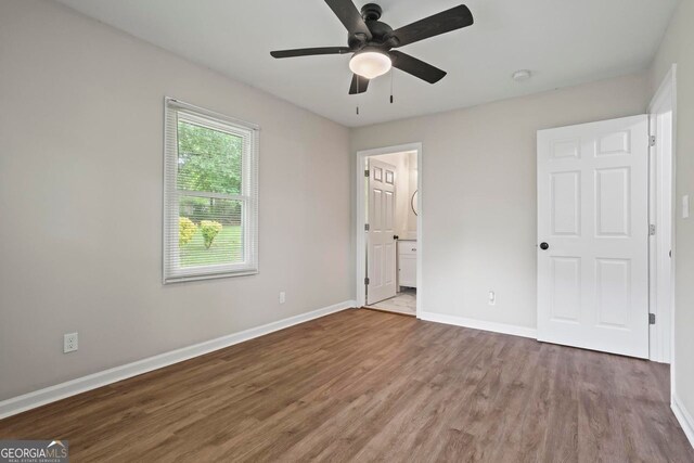 unfurnished bedroom featuring baseboards, ensuite bath, wood finished floors, and ceiling fan
