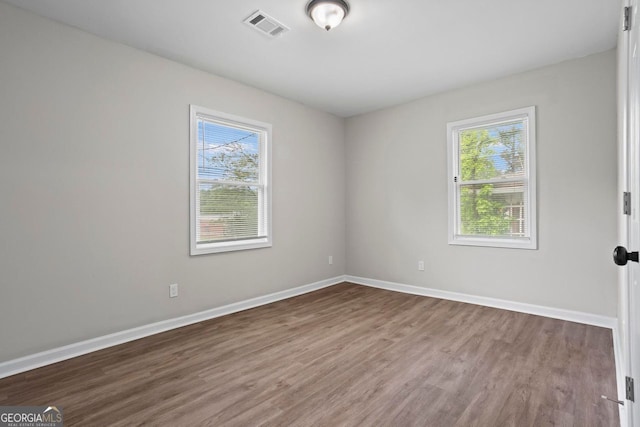 spare room with baseboards, visible vents, a healthy amount of sunlight, and wood finished floors