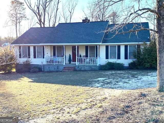 ranch-style house featuring covered porch, roof with shingles, a front lawn, and a chimney