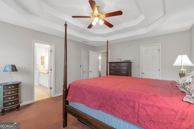 carpeted bedroom featuring a tray ceiling, connected bathroom, visible vents, and baseboards